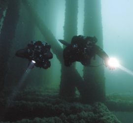 two properly weighted divers float between the legs of a pier